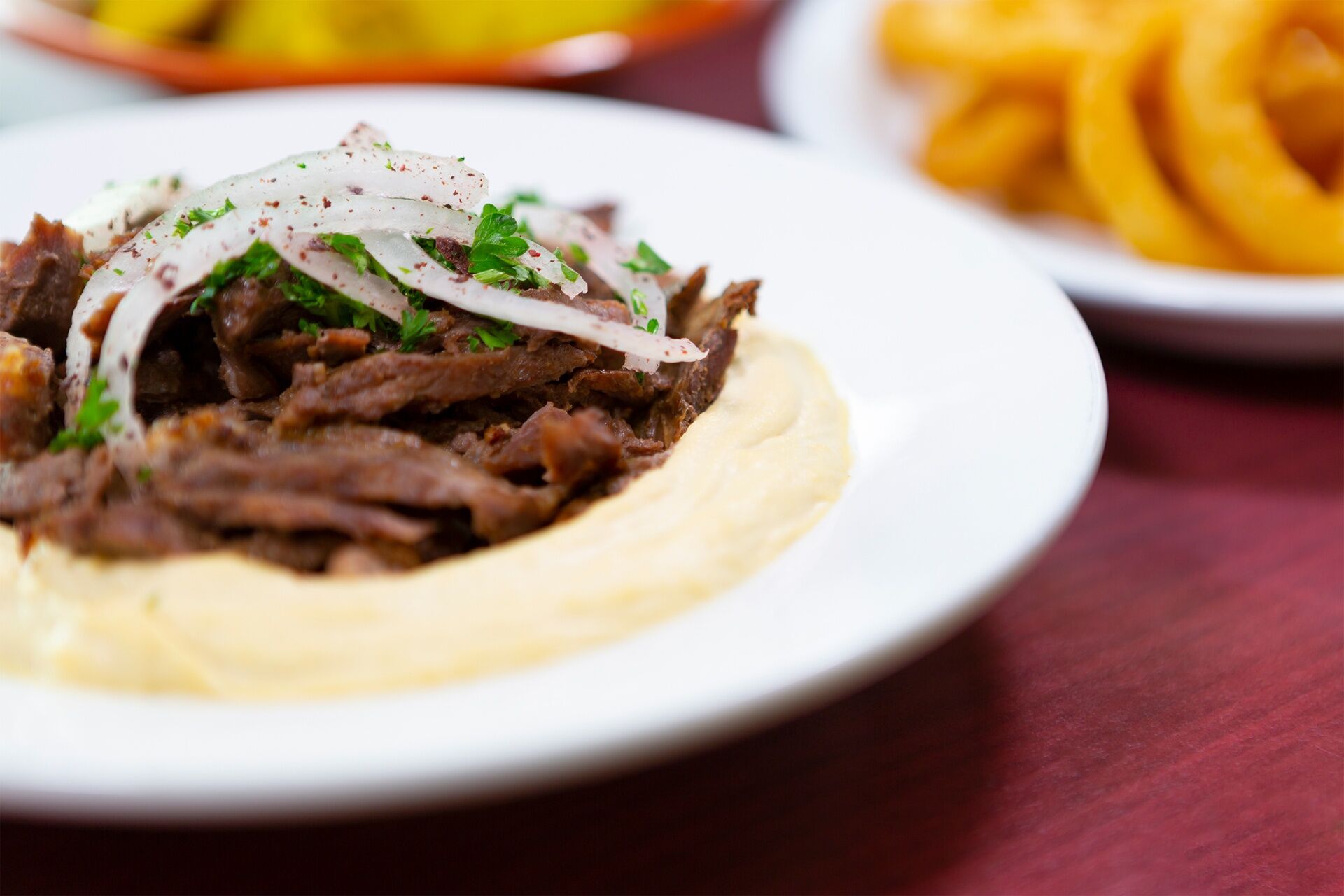 Beef shawarma plated over hummus with onions and parsley